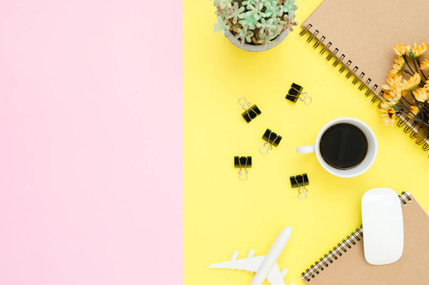 Flat lay design of travel summer concept - Top view of notebook, airplane, tree, flower, coffee, clip and wireless mouse on pink and yellow pastel color copy space. travel on pastel color background. - Фото, изображение