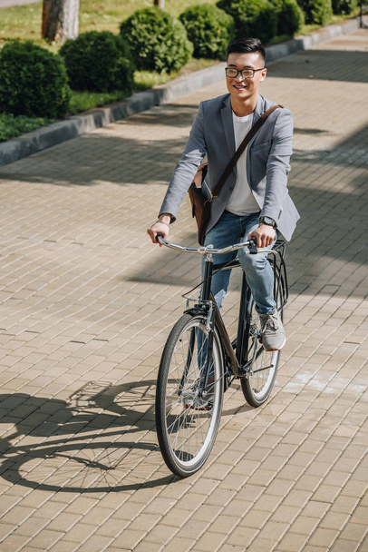 komea hymyilevä aasialainen mies pyöräily pyörällä kaupungissa
 - Valokuva, kuva