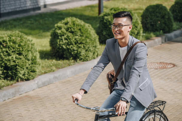 smiling asian man riding bicycle in park - Фото, изображение