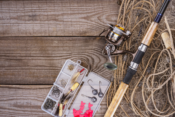 piatta con rete da pesca, canna da pesca e scatola di plastica con attrezzatura da pesca e ganci su assi di legno
  - Foto, immagini