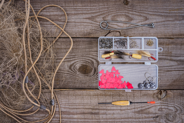 vista sopraelevata di rete da pesca e scatola di plastica con attrezzatura da pesca e ganci su fondo di legno
  - Foto, immagini