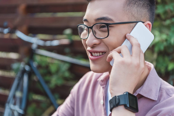 smiling asian man in eyeglasses talking on smartphone - Foto, Bild