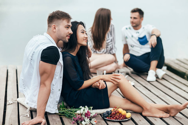 Happy couples having fun resting by river. Picnic on pier. - Foto, afbeelding