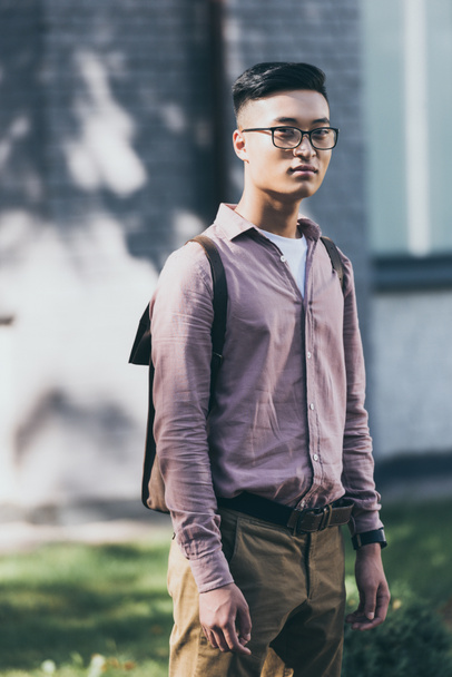portrait of pensive asian man in eyeglasses looking at camera on street - Photo, Image