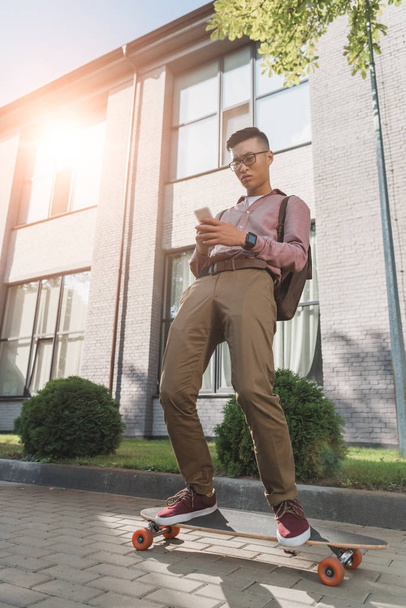 зосереджений азіатський чоловік використовує смартфон, стоячи на дошці на вулиці
 - Фото, зображення