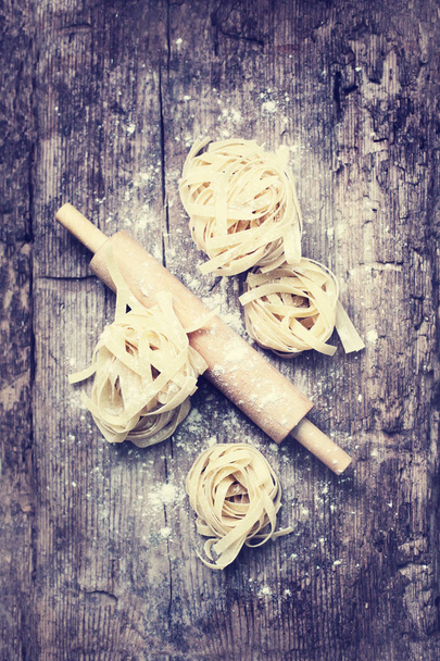 fettuccine nests with rolling-pin on wooden background - Foto, Imagem
