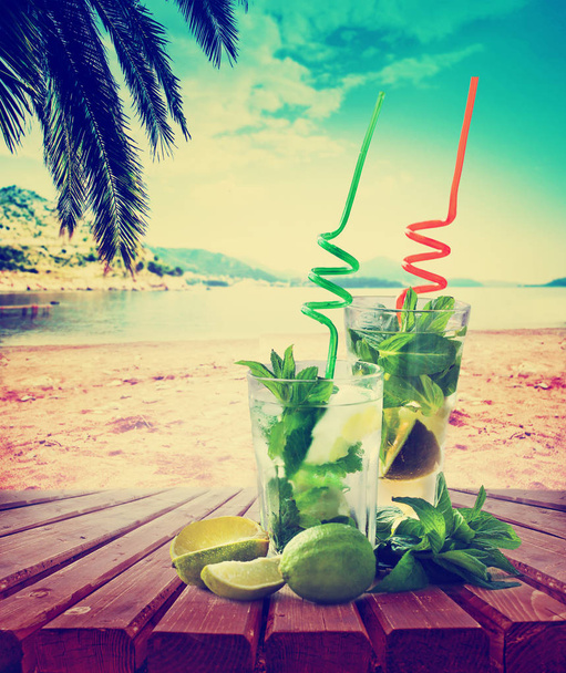 mojito cocktails with straws on wooden table with beach on background - Foto, Imagem