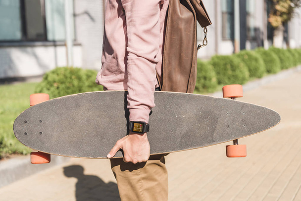 gedeeltelijke weergave van man met rugzak longboard houden op straat - Foto, afbeelding
