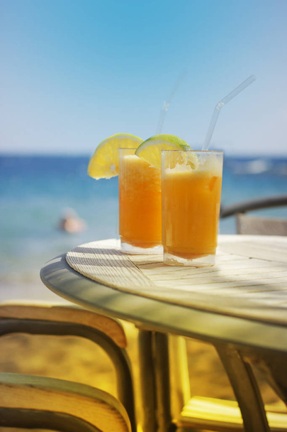two glasses of tasty orange juice over table at beach - Foto, afbeelding
