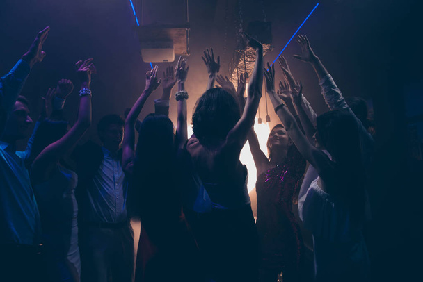 Back behind rear view photo of a silhouette of careless, excited ecstatic delightful carefree persons dancers on a dance floor raised hands up - 写真・画像