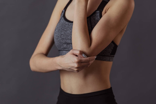 Cropped image of girl in sportswear touching her elbow feeling pain, on gray background - Photo, Image