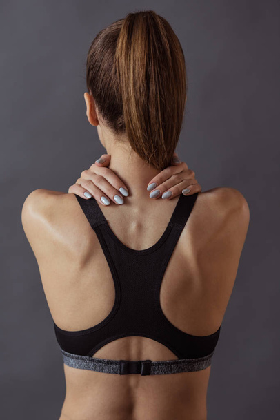 Back view of beautiful girl in sportswear touching her neck, on gray background - Valokuva, kuva
