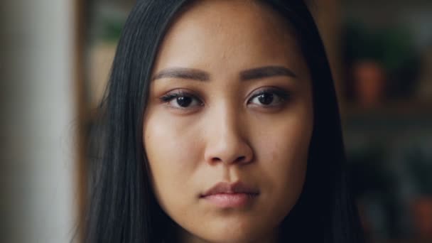 Close-up slowmotion portrait of attractive young Asian woman with perfect skin looking at camera with straight face then smiling showing white teeth. - Materiał filmowy, wideo