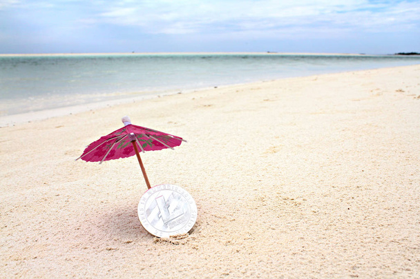 Hopeinen litecoin paperin alla sateenvarjo rannalla, matala painopiste
 - Valokuva, kuva
