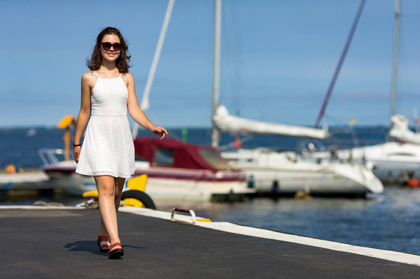 Young girl in white dress and sunglasses posing at seaside - Foto, immagini