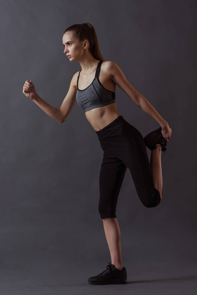 Full length portrait of beautiful girl in sportswear stretching, on gray background - Foto, Imagem
