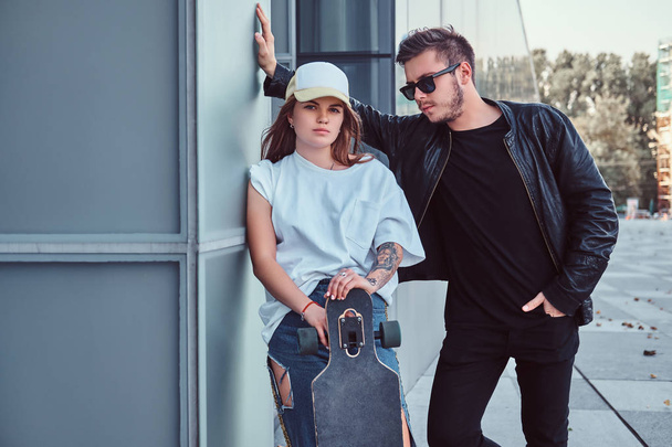 Приваблива молода пара, одягнена в модний одяг, позує зі скейтбордами біля хмарочоса
. - Фото, зображення