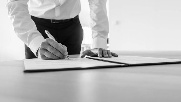 Сірий образ бізнесмена, що стоїть за своїм столом підписання контракту або юридичного документа
. - Фото, зображення