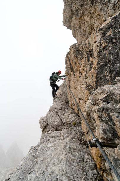 junge Bergsteigerin an einer steilen und exponierten Felswand beim Klettern eines Klettersteigs - Foto, Bild