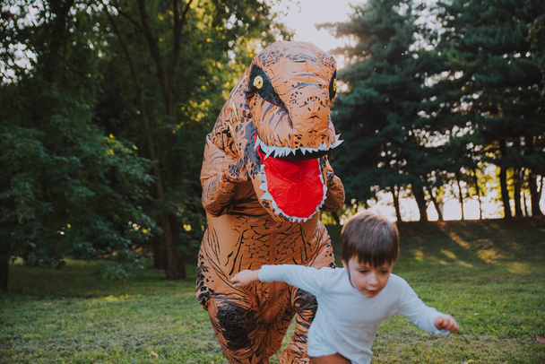 Πατέρας και γιος που παίζουν στο πάρκο, με ένα κοστούμι δεινόσαυρος, τη διασκέδαση με την οικογένεια υπαίθρια - Φωτογραφία, εικόνα