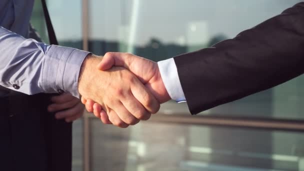 Dolly shot of two businessmen shaking hands after successful deal near office building. Close up of young colleagues congratulating each other in urban environment. Handshake of business partners - Footage, Video