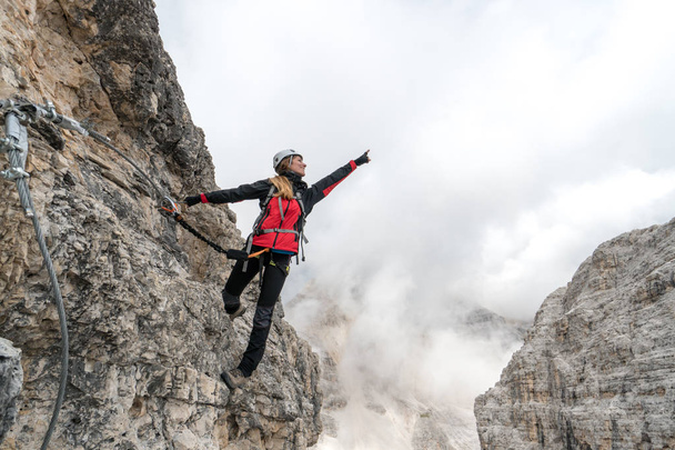 молодая женщина-альпинистка на вертикальной и открытой скале, взбирающаяся на Виа Феррата - Фото, изображение