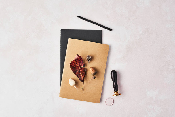 Autumn concept of the office. Top view of twok notebooks with leaf, acorn, wax seal stamp and black pencil on rose and white background. Flat lay with copy space. - Photo, Image