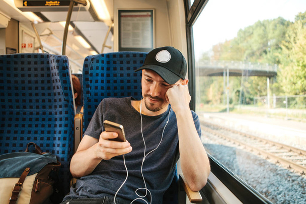 ein junger Mann hört Musik oder Podcast, während er im Zug unterwegs ist - Foto, Bild