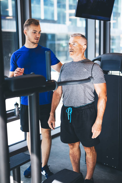 Personal trainer giving instructions to older man at the gym. Physical activity of senior people. - Photo, Image