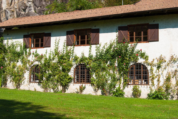 Velha casa individual em dois andares e rosas e grande gramado da frente
 - Foto, Imagem