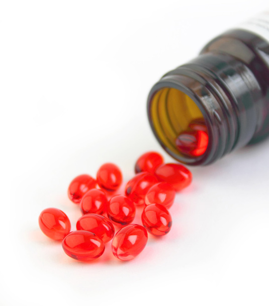 Pílulas de vitamina vermelha com garrafa marrom no fundo branco
 - Foto, Imagem