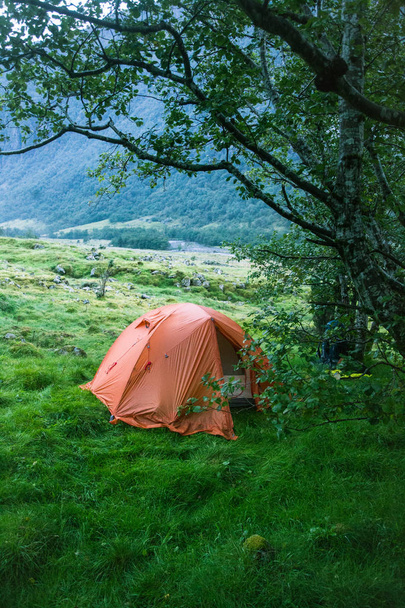 Una tienda de campaña naranja durante un viaje de senderismo en el Parque Nacional Folgefonna, Noruega. Dormir en tienda de campaña en las montañas. Otoño nublado
. - Foto, Imagen