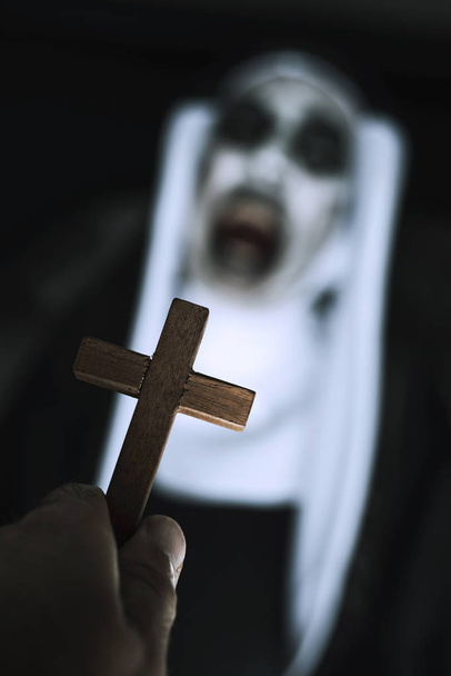fechar uma cruz na mão de um homem e uma freira do mal assustador, vestindo um hábito típico preto e branco, gritando
 - Foto, Imagem