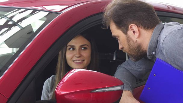 Mujer atractiva sentada en un coche nuevo hablando con el vendedor
 - Foto, imagen