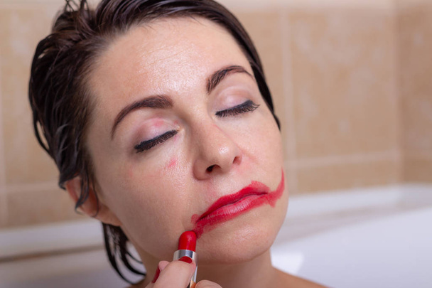 dépression féminine. une femme dans la salle de bain avec un regard pétrifié coupe le rouge à lèvres sur son visage
. - Photo, image