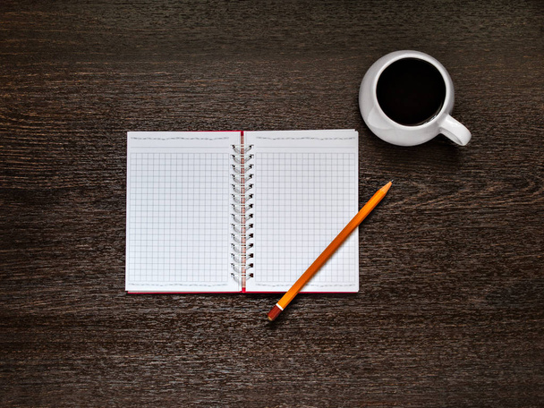 On a wooden background there is an open notebook, a yellow pencil, a white cup with coffee. Horizontally with copy space - Foto, imagen