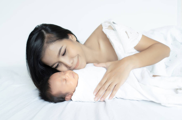 ベッド、マタニティの概念、美しい家族、母の日のコンセプトのソフトな画像で眠っている新生児の赤ちゃんにキス若いアジアの母. - 写真・画像