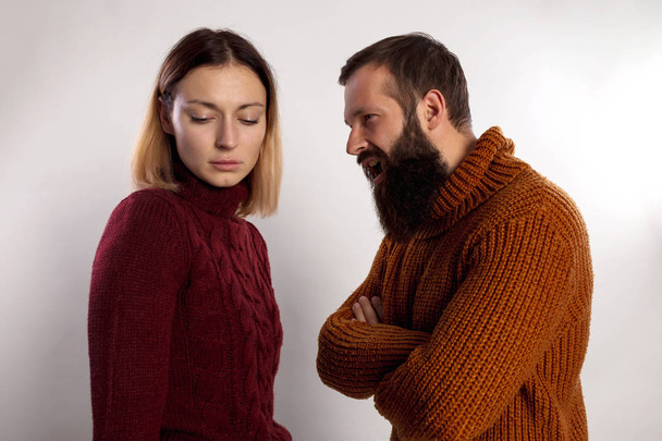 Young bearded man screaming against a sad young woman both dressed in warm knitted sweaters. Isolated gray background - Fotó, kép