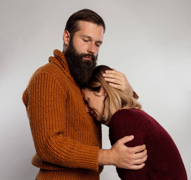 Bearded handsome man hugging his sad girlfriend, beautiful woman is upset. Man comforting his sad mourning friend embracing her. Conflict and emotional stress in young people couple relationship - Photo, Image