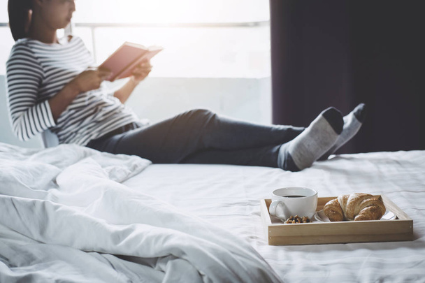 Relaxation and recreation, Young happiness woman on the bed with enjoying reading old book in holiday and morning cup of coffee and Croissant. - Foto, Imagem