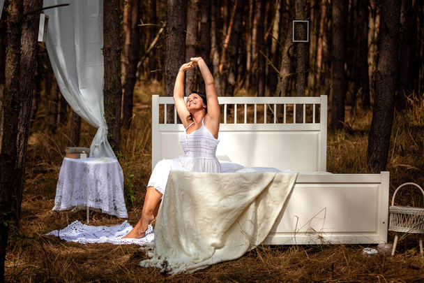 Vrouw wordt wakker in bed in de ochtend op de achtergrond van de natuur van bos - Foto, afbeelding