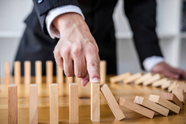 Wooden game strategy, Businessman hand stopping falling wooden dominoes effect from continuous toppled or risk, strategy and successful intervention concept for business. - Foto, afbeelding