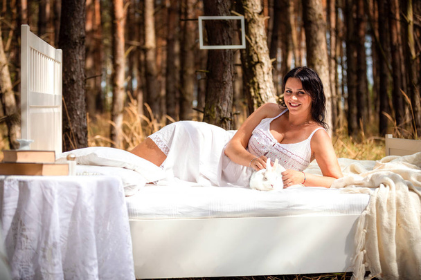 Жінка з кроликом в ліжку вранці на природі на фоні лісу
 - Фото, зображення