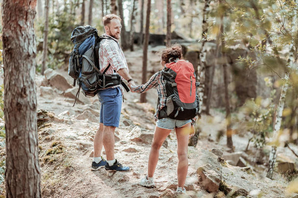 Bearded man with backpack supporting his tender woman while hiking - Foto, afbeelding