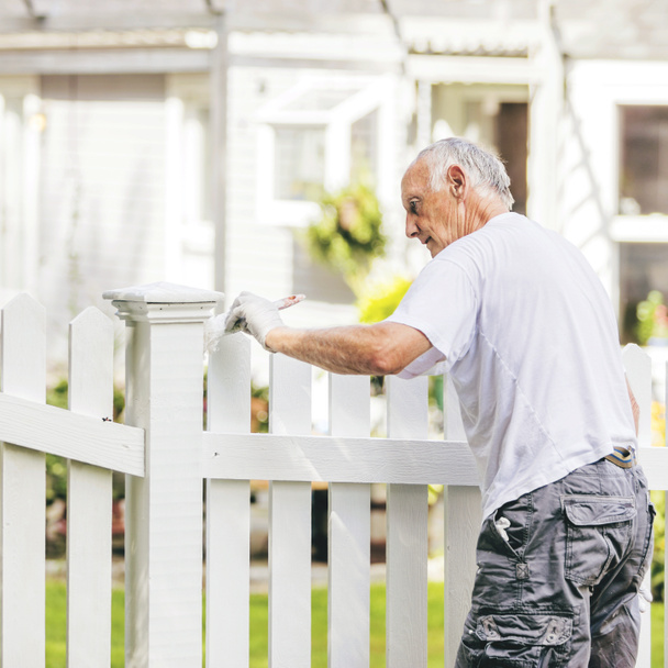 Homme âgé actif peignant une clôture de piquet blanc avec tonification chaude
 - Photo, image