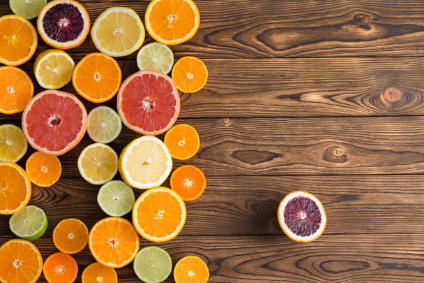 Ζωηρόχρωμη επίδειξη μιας ποικιλίας των περικοπών εσπεριδοειδή με πορτοκάλια, γκρέιπφρουτ, μανταρίνι, ασβέστης, λεμόνι και το αίμα τα πορτοκάλια με ένα ενιαίο πορτοκαλί αίμα οριστεί στο πλάι σε φόντο ξύλινη - Φωτογραφία, εικόνα