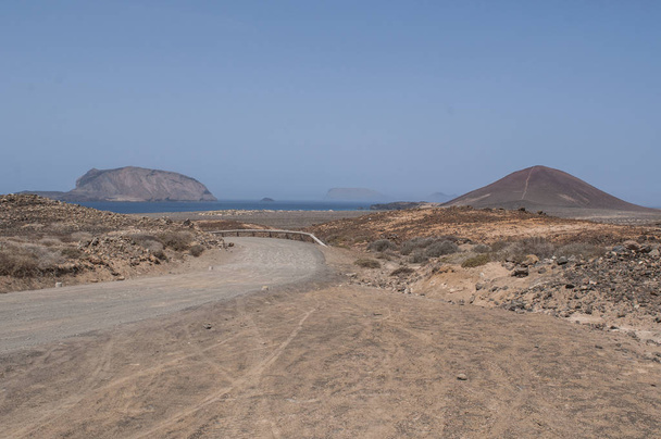 Canary Islands, 12 / 09 / 2018: the dirt road to the beach Playa de Las Conchas and volcano Montana Bermeja (Scarlet Mountain) of La Graciosa, the main archipelago island Chinijo, northwest of Lanzarote
 - Фото, изображение