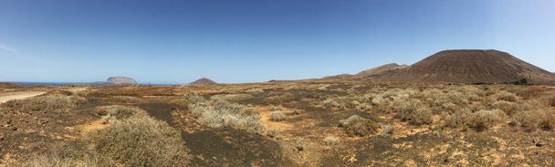 Lanzarote, Canarische eilanden, 12/09/2018: zandweg, bush desertic landschap naar Montana Pedro Barba, twin-summitted en de twin-gekraterde vulkaan van La Graciosa, de belangrijkste archipel eiland Chinijo - Foto, afbeelding