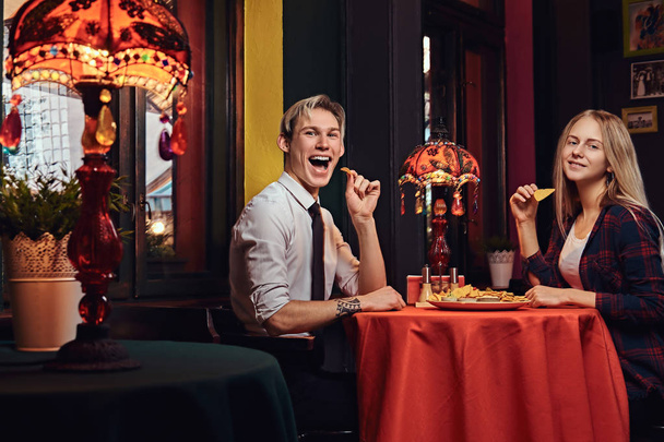 メキシコ料理のレストランでデート中にナチョスを食べて魅力的なカップル.  - 写真・画像