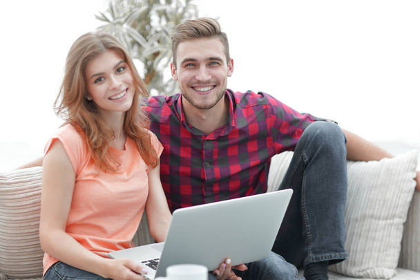 young couple of students uses a laptop sitting on sofa - Fotografie, Obrázek